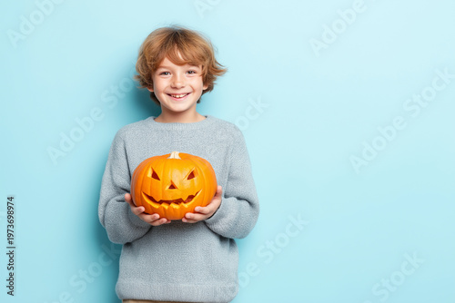Happy child holding a carved pumpkin by a blue wall