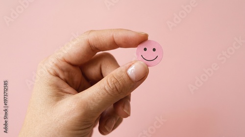 Hand Holding Smiley Face: A close-up shot of a hand gently holding a small, pink smiley face against a soft, pastel backdrop, evoking feelings of positivity and well-being.