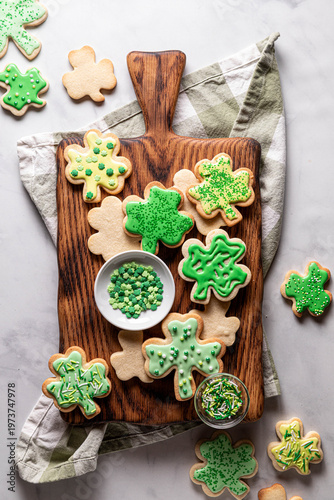 An assortment of decorated shamrock shaped sugar cookies on a wooden board.