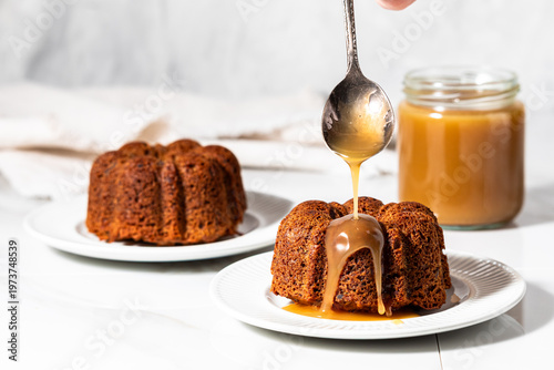 A spoon drizzling caramel sauce on baked sticky toffee pudding cakes.