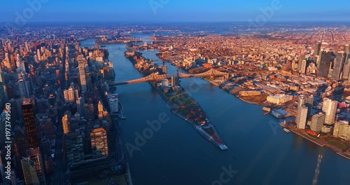 Footage above the East River approaching the Queensboro Bridge. Cityscape of Queens is lit by the setting sun.