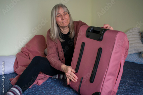 Senior woman lifting packed suitcase ready for travel at home