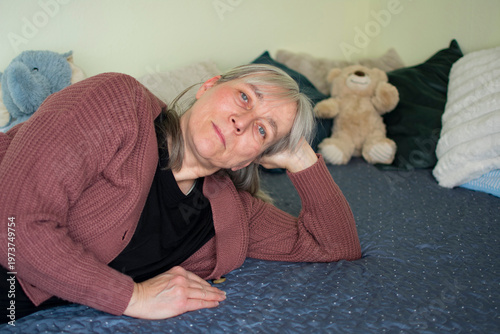 Mature woman lying on bed looking at camera feeling lonely at home