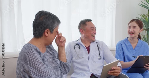 Senior Asian doctor laughing while holding a digital tablet in a bright clinic room, focusing on empathetic elderly care, positive patient experiences, and friendly healthcare communication.