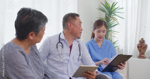 Senior Asian doctor explains tablet data to elderly female patient in a clinic, focusing on senior healthcare, patient communication, and modern medical technology.
