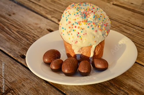 Easter cake Paska with icing and chocolate eggs on wooden background.