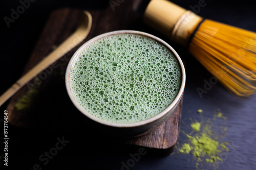 Matcha tea with fine foam texture in a cup, styled with traditional bamboo whisk, spoon.