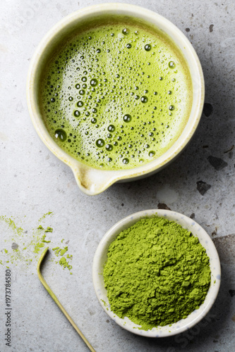 Bowl of matcha green tea with creamy foam, styled with bamboo spoon and powder.