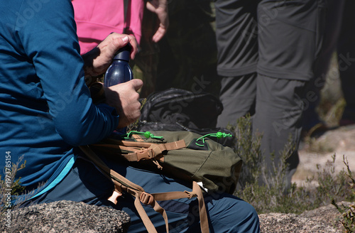 Hiker resting and taking a water bottle out of the backpack, he is opening it do drink, mountain trail