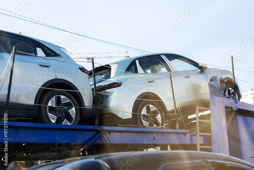 Shiny silver sports utility vehicles arranged on carrier truck in open freight yard