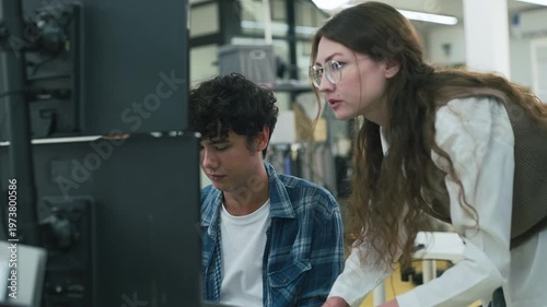 collaborative AI development team in modern tech office: young male developer coding on laptop while senior colleague leans over discussing code and data visualizations on multiple monitors	