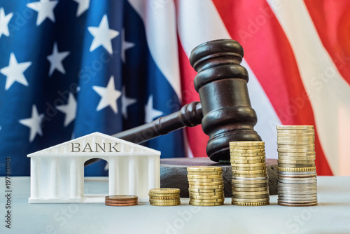 A model of a bank building with a gavel, growing stacks of coins against of the US flag. Financial regulation, taxation, economic policy, business loans, credits in America. Business investment