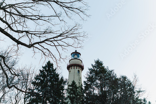 Fotografie Lighthouse stands in a forest during the day with bare branches and green trees