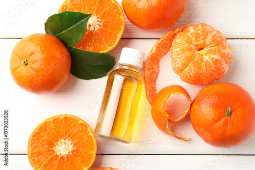 Bottle of tangerine essential oil and fruits on white wooden table, flat lay