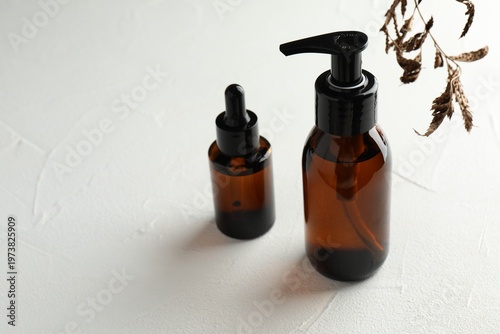 Bottles of cosmetic product and dry leaves on light table, closeup. Space for text