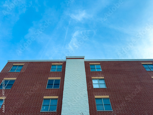 Looking up at a red brick building under a blue sky with a few clouds in the late afternoon hours