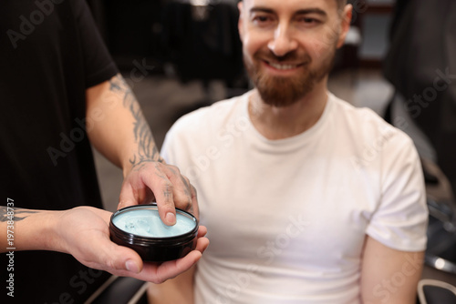 Фотография Barber with styling product and his client indoors, closeup