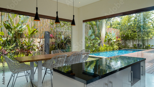A modern kitchen with a black countertop and a large window overlooking a pool. The room is filled with natural light and has a sleek, minimalist design