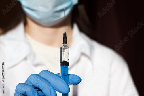 A doctor in a medical gown and gloves holds a syringe with an injection drug. Medicine and treatment