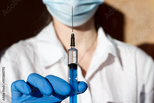Medical worker in white coat, mask and gloves holding a syringe
