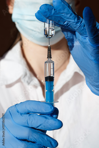 A doctor with a syringe in his hands draws up a solution for injection. Syringe and ampoule in his hands, closeup. Preparation for the procedure
