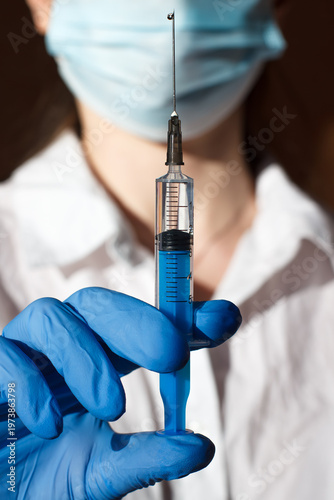 Syringe with injection drug in hands of medical worker. Man in medical gloves, mask and white medical coat. Closeup photo