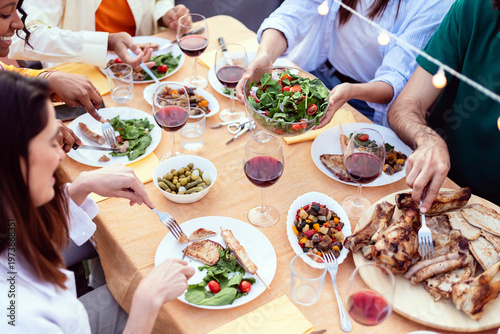 Canvas Print Diverse friends sharing food and drinks at a festive summer dinner party on an o