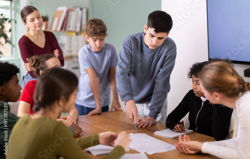 At round table meeting, teen participants discuss problem and try to find solution, teacher watching. Brain storm, team discussion, personal growth courses, psychological training, collegiate council