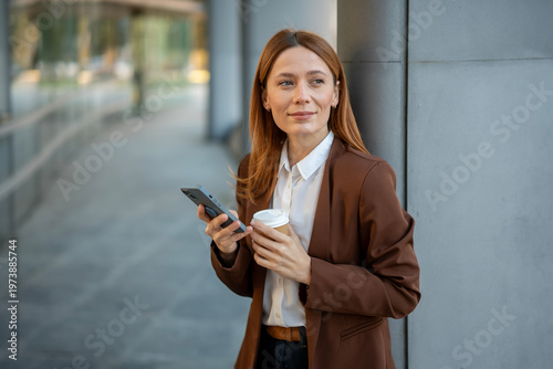 Businesswoman holding smartphone and coffee thinking about work