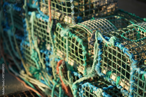 Crab traps are neatly stacked on a fishing boat docked by the coast. The early morning sunlight casts a warm glow on the traps, highlighting their vibrant colors and textures.