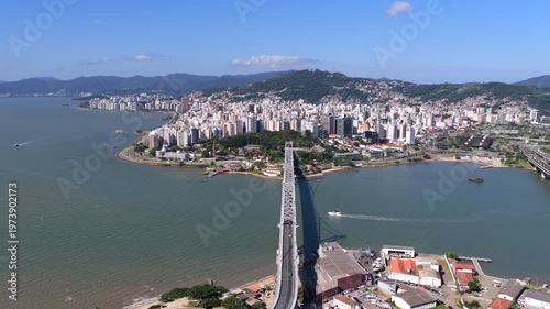 Drone flying forward over Hercilio Luz Bridge revealing Florianopolis skyline and bay with boat movement.