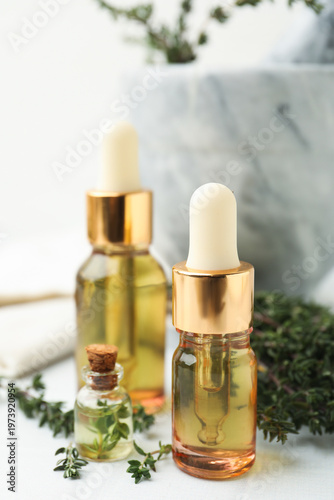 Thyme essential oil and fresh herbs on white table, closeup