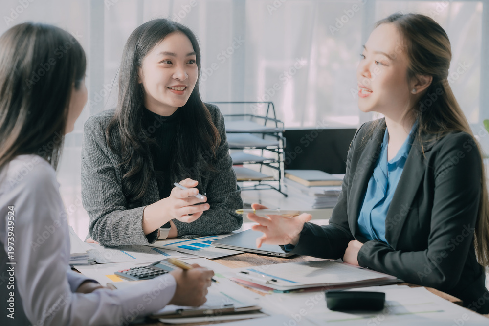 Fototapeta premium Three Asian businesswomen collaborate with business partners using laptop technology and graphical documents in a conference room of an office.