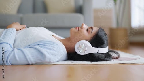 Young Asian woman relaxing at home. Girl in headphones listen to music in cozy living room, using audio healing apps for mental health. Female wellness and self-care lifestyle, ASMR sound therapy