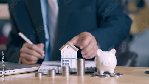 Businessman signing documents and showing house model for mortgage loan approval success.
