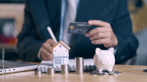 Businessman holding credit card and signing house purchase agreement with focus on home model.
