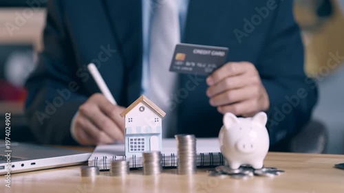 Businessman holding credit card and signing house purchase agreement with focus on home model.