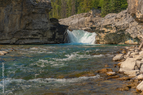 Scenic summer landscape of Elbow Falls in Kananaskis Country, Alberta, Canada. Beautiful waterfall cascading over rocky cliffs into the Elbow River with evergreen pine forest and blue sky Canada