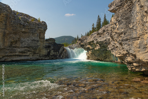 Scenic summer landscape of Elbow Falls in Kananaskis Country, Alberta, Canada. Beautiful waterfall cascading over rocky cliffs into the Elbow River with evergreen pine forest and blue sky Canada