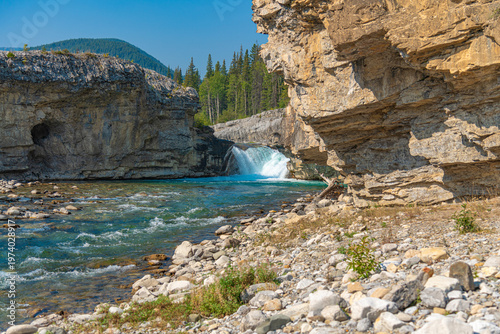 Scenic summer landscape of Elbow Falls in Kananaskis Country, Alberta, Canada. Beautiful waterfall cascading over rocky cliffs into the Elbow River with evergreen pine forest and blue sky Canada