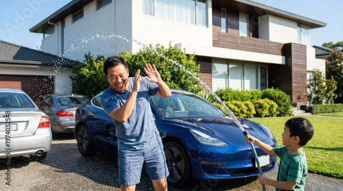 Asian Father and Son Washing Car Together, Playful Family Moment in Modern Home Driveway