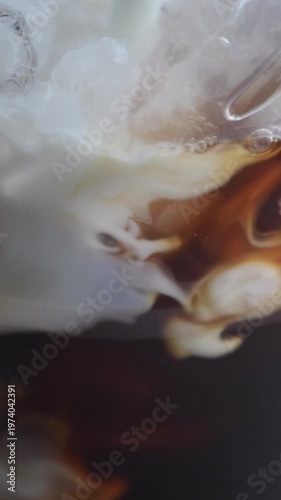 4K Vertical video Iced coffee with milk pouring into glass creating smooth swirl with ice cubes Refreshing cold beverage,Concept with rich texture ideal for cafe summer drink and commercial advertisin