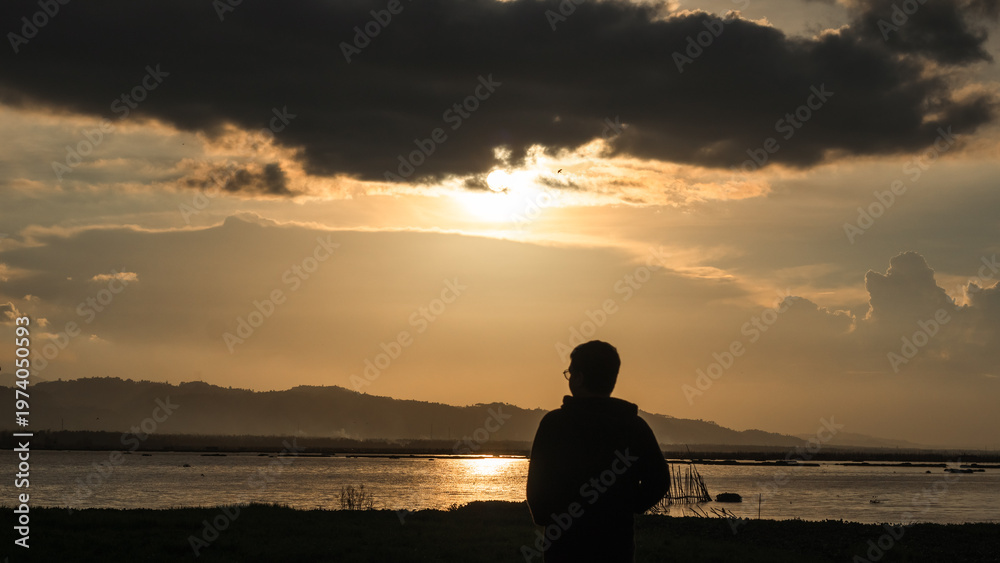 Fototapeta premium Man Silhouetted Against Golden Sunset Over Water