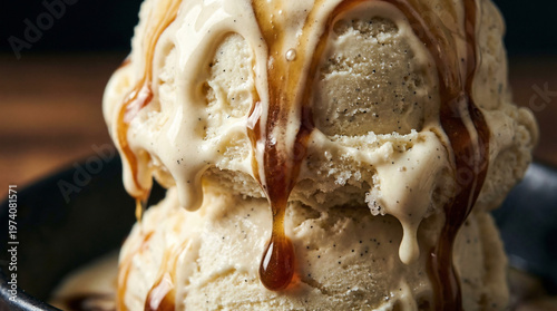 Ice cream scoops with caramel sauce in dark bowl on wooden table  