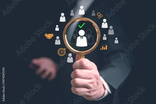 Hand hold magnifying glass highlighting selected candidate icon with check mark among group of people symbol, representing recruitment, talent acquisition, human resource screening and hiring process.