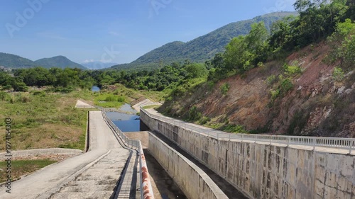 Hydraulic canal and mountain landscape merge through long concrete structure. Open water channel runs along valley toward distant hills. This hydraulic canal provides drainage for mountain landscape.