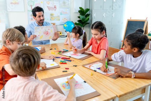 The teacher hold the picture that is the creation from kid in the classroom and give rating also ask for the idea and explaination from the owner.