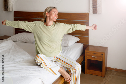 Happy Refreshed Woman waking up from Bed in the Morning by Stretching hand