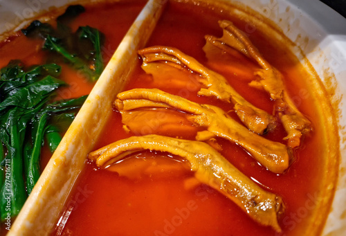 Close-up of tender braised duck feet in a rich savory red sauce, served in a divided ceramic pot with fresh green vegetables