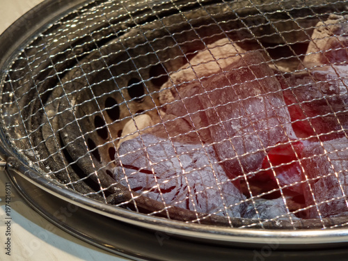 Close-up of a charcoal grill with glowing hot red coals under a metal wire mesh, ready for Japanese or Korean BBQ
